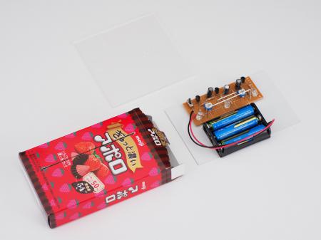 基板と電池ボックスはお菓子の箱の中におさめるよ。基板にはアクリル板ホルダーをつけるので、ケースとなる箱にはアクリル板が差し込めるようにスリットを入れている。